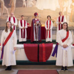 Piispa messuavustajineen seisoo alttarilla, kaiteen edessä vihittävät kasvot messuyleisöön päin.